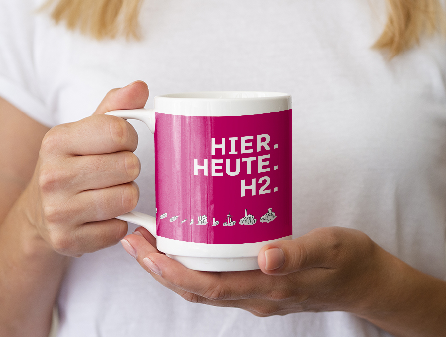 Foto einer Person, die einen Becher in die Kamera hält mit der Aufschrift "Hier. Heute. H2."